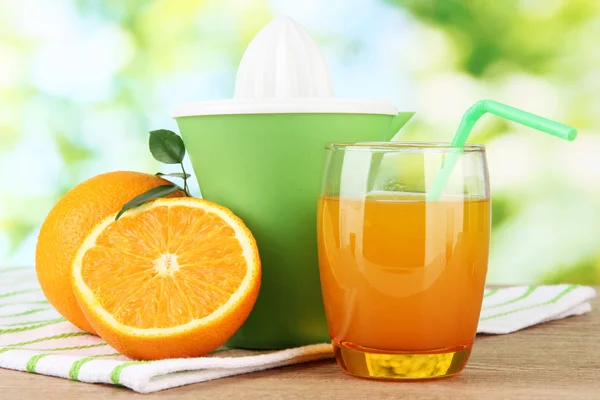 Citrus press, glass of juice and ripe oranges on brown wooden table — Stock Photo, Image