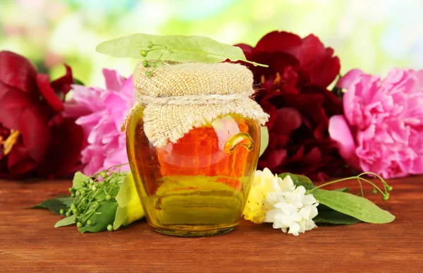 Honigglas mit Blüten aus Linde, Akazie, Pfingstrose auf Holztisch, auf hellem Hintergrund — Stockfoto