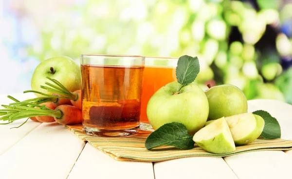 Glas juice, äpplen och morötter på vita träbord, på grön bakgrund — Stockfoto