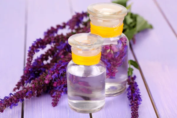 Medicine bottles with salvia flowers on purple wooden background — Stock Photo, Image