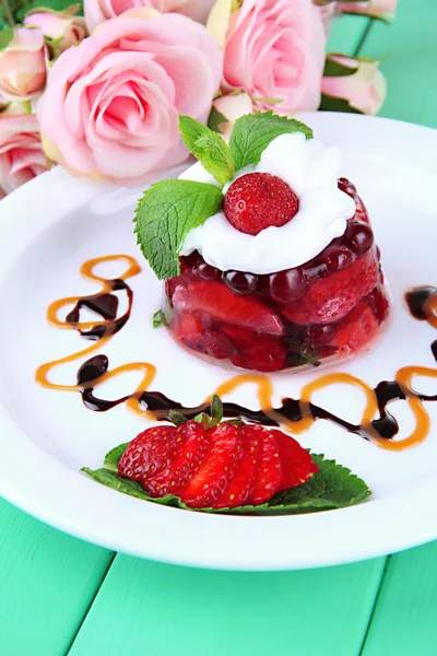 Sabroso postre de gelatina con bayas frescas, sobre fondo de rosas rosadas — Foto de Stock