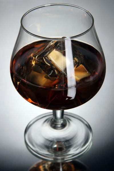 Brandy glass with ice on grey background — Stock Photo, Image