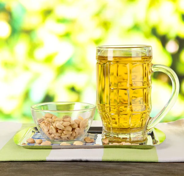 Beer in glass and nuts on tray on wooden table on nature background — Stock Photo, Image