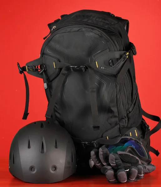 Winter sport glasses, helmet and gloves, backpack, on red background — Stock Photo, Image