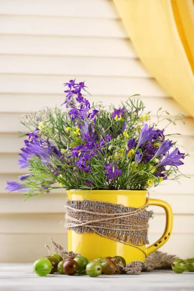 Bellissimo bouquet di fiori di campo in tazza e bacche su tavolo di legno — Foto Stock