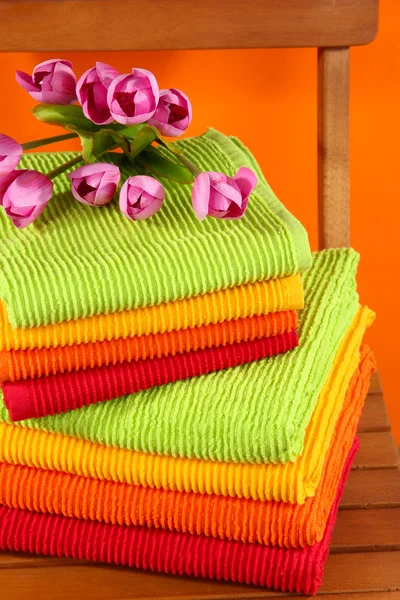 Handdukar och blommor på trä stol på orange bakgrund — Stockfoto