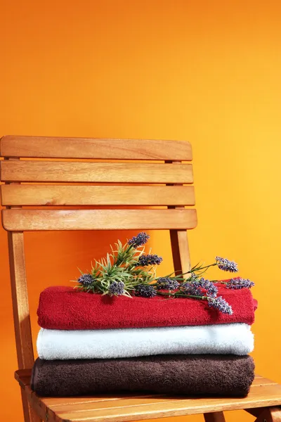 Towels and flowers on wooden chair on orange background — Stok fotoğraf