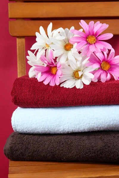 Towels and flowers on wooden chair on brown background — Stock Photo, Image