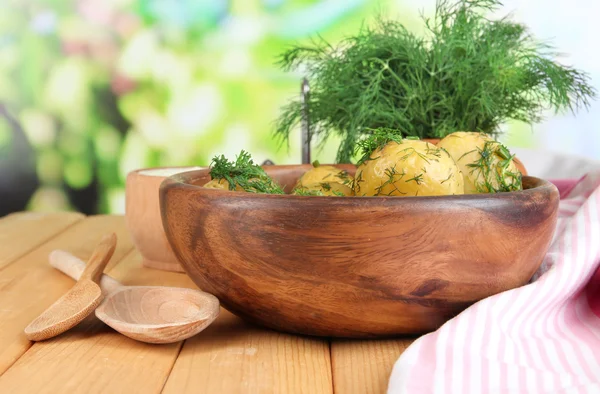 Boiled potatoes on wooden bowl near napkin on wooden table on nature background — Stock Photo, Image