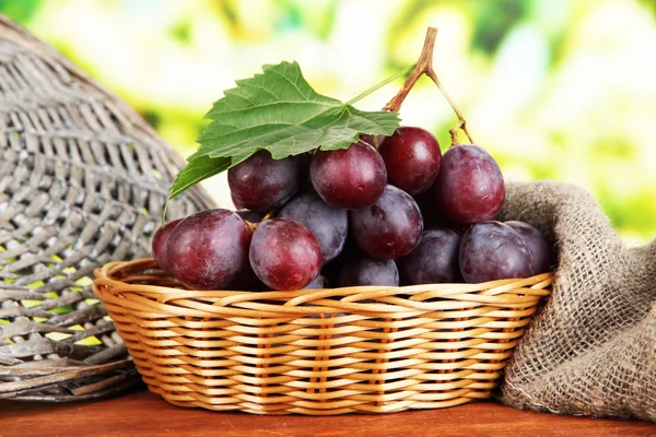 Maturare deliziose uve in cesto di vimini sul tavolo su sfondo luminoso — Foto Stock