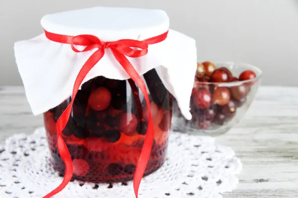 Yummy jam in bank on napkin on wooden table on gray background — Stock Photo, Image