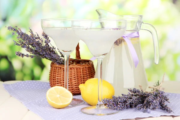 Lavender lemonade in glass jug and cocktail glasses, on bright background — Stock Photo, Image