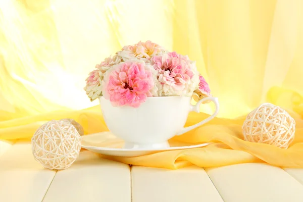 Roses en tasse sur table en bois sur fond de tissu jaune — Photo