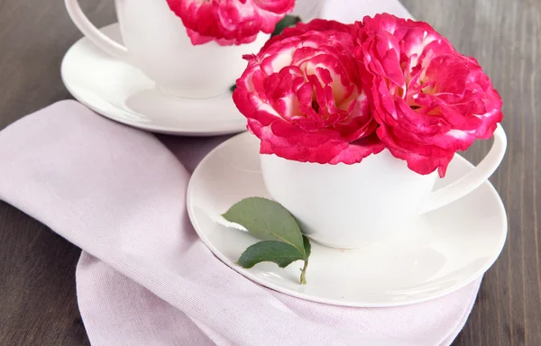 Розы в чашках на салфетке на деревянном фоне — стоковое фото