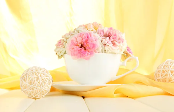 Rosas en copa sobre mesa de madera sobre fondo de tela amarilla — Foto de Stock