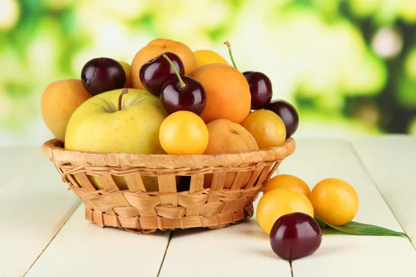 Světlé letní ovoce v košíku na dřevěný stůl na přírodní pozadí — Stock fotografie