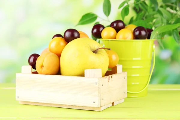 Bright summer fruits in pail and wooden box on wooden table on natural background — Stock Photo, Image