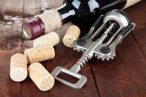 Sacacorchos con tapones de vino y botella de vino sobre mesa de madera —  Fotos de Stock