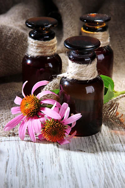 Medicine bottles with purple echinacea flowers on wooden table with burlap — Stock Photo, Image