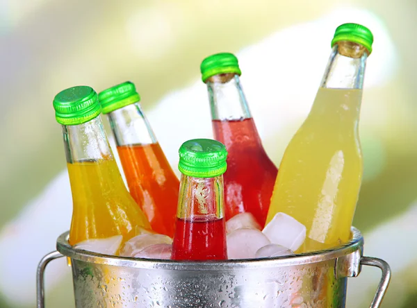 Бутылки с вкусными напитками в ведре с кубиками льда, на ярком фоне — стоковое фото