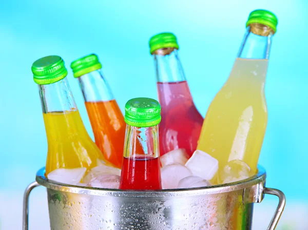 Μπουκάλια με νόστιμα ποτά σε κουβά με παγάκια, στο φωτεινό φόντο — Φωτογραφία Αρχείου