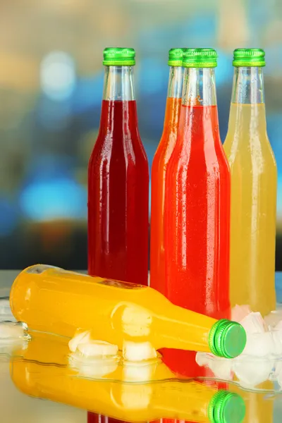 Bottles with tasty drinks with ice cubes, on bright background — Stock Photo, Image