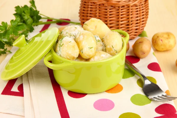 Tender young potatoes with sour cream and herbs in pan on wooden table close-up — Stock Photo, Image