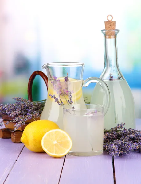 Levandule limonády v láhvi a džbán na fialové dřevěný stůl, na světlé pozadí — Stock fotografie