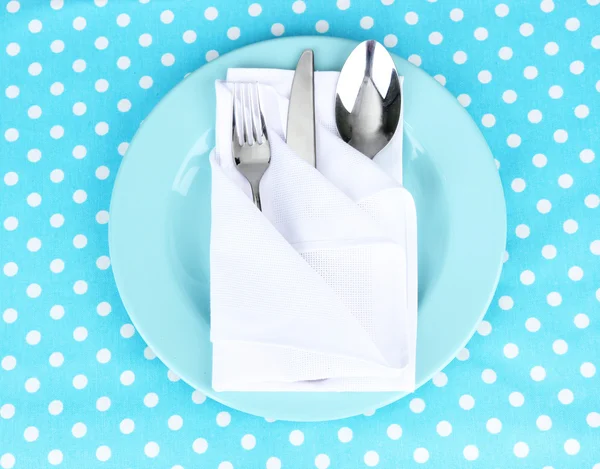 Folded napkin with fork, spoon and knife, on plate, on color background — Stock Photo, Image