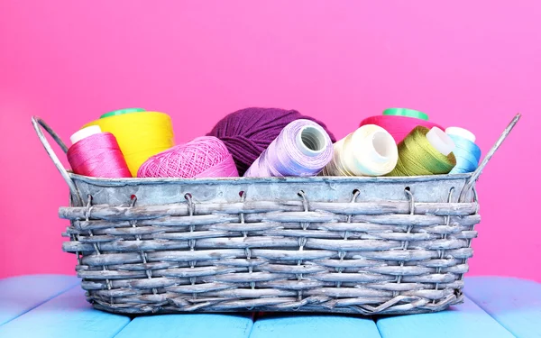 Bright threads in basket on wooden table on pink background — Stock Photo, Image