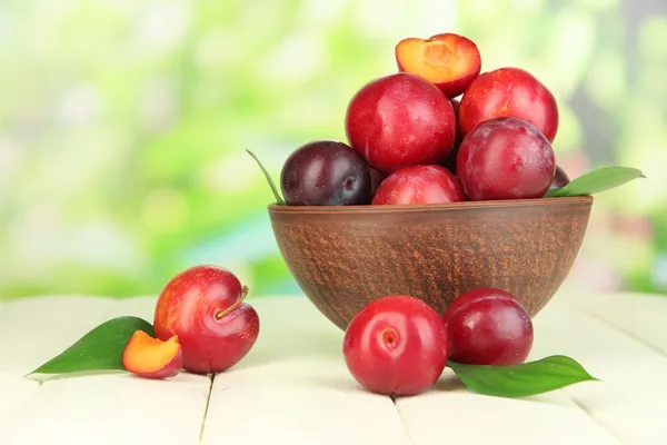 Ripe plums in bowl on wooden table on natural background — Stock Photo, Image