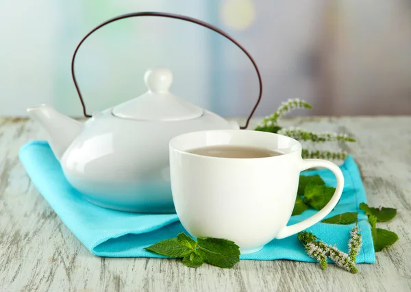 Teekanne und Tasse Kräutertee mit frischen Minzblüten auf Holztisch — Stockfoto