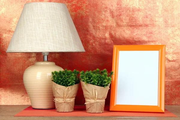 Marco de fotos colorido, lámpara y flores en la mesa de madera sobre fondo rojo — Foto de Stock