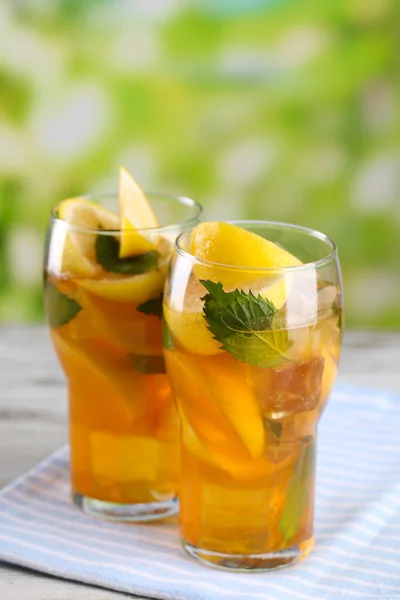 Холодный чай с лимоном и мятой на деревянном столе, на открытом воздухе — стоковое фото