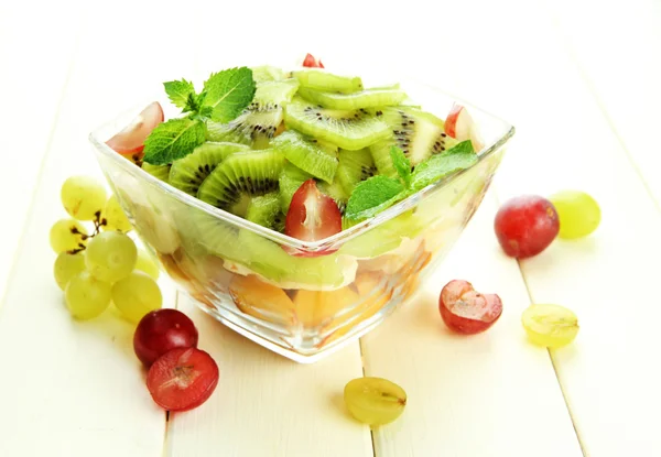 Chutný ovocný salát ve skleněné míse, na bílý dřevěný stůl — Stock fotografie