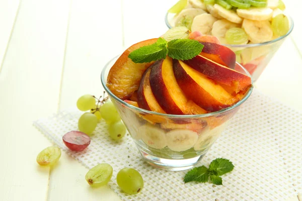Salada de frutas saborosas em tigelas de vidro, em mesa de madeira branca — Fotografia de Stock