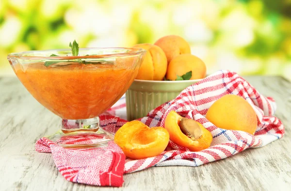 Confiture d'abricots dans un bol en verre et abricots frais, sur table en bois, sur fond lumineux — Photo