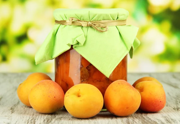 Marmellata di albicocche in vaso di vetro e albicocche fresche, su tavolo di legno, su sfondo brillante — Foto Stock