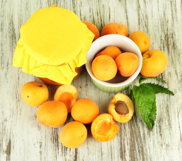 Fresh apricots and apricot jam in jar, on wooden table, on bright background — Stock Photo, Image