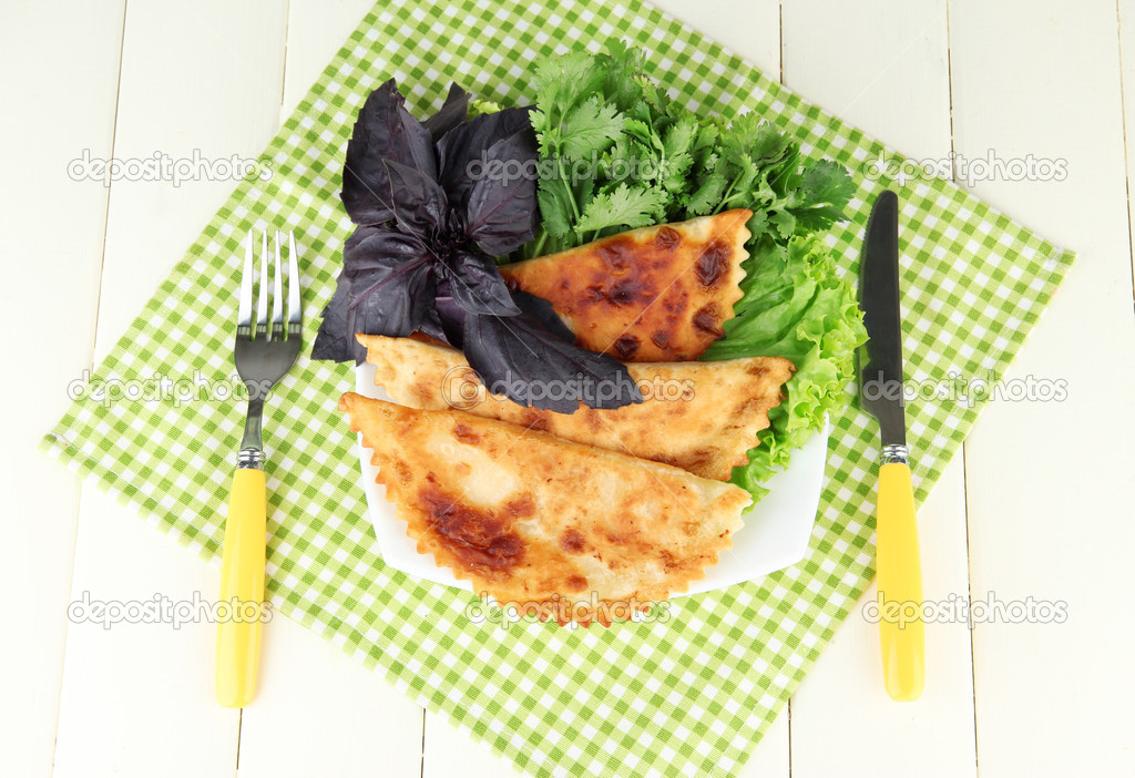 Tasty chebureks with fresh herbs on plate,on color wooden background