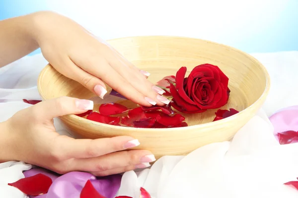 Woman hands with wooden bowl of water with petals, on blue background — Stock Photo, Image