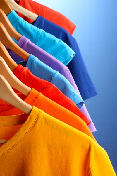 Lots of T-shirts on hangers on blue background — Stock Photo, Image