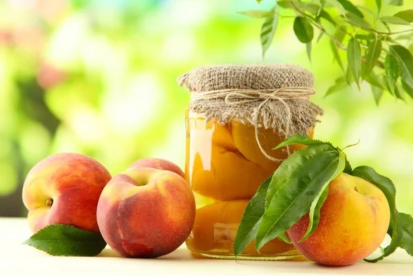 Jar of canned peaches and fresh peaches on wooden table, outside