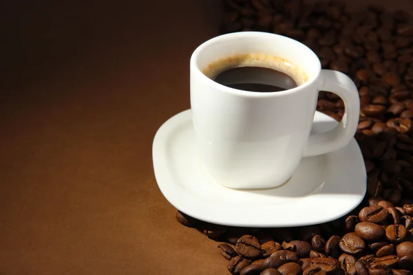 Taza de café con granos de café sobre fondo marrón —  Fotos de Stock