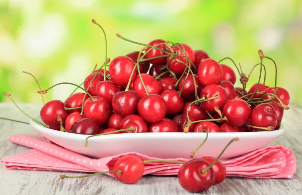 Cherry berries on plate on wooden table on bright background — Stock Photo, Image