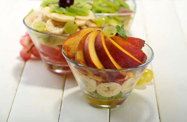 Ensalada de frutas sabrosas en cuencos de vidrio, sobre mesa de madera blanca —  Fotos de Stock