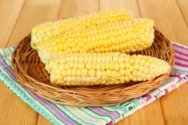 Fresh corn on wicker mat, on wooden background — Stock Photo, Image