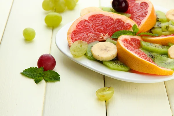 Assortment of sliced fruits on plate, on white wooden table — Stock Photo, Image