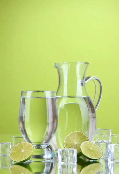 Glas tillbringare med vatten och glas på grön bakgrund — Stockfoto