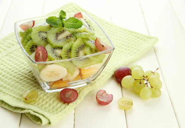 Salada de frutas saborosas em tigela de vidro, na mesa de madeira branca — Fotografia de Stock